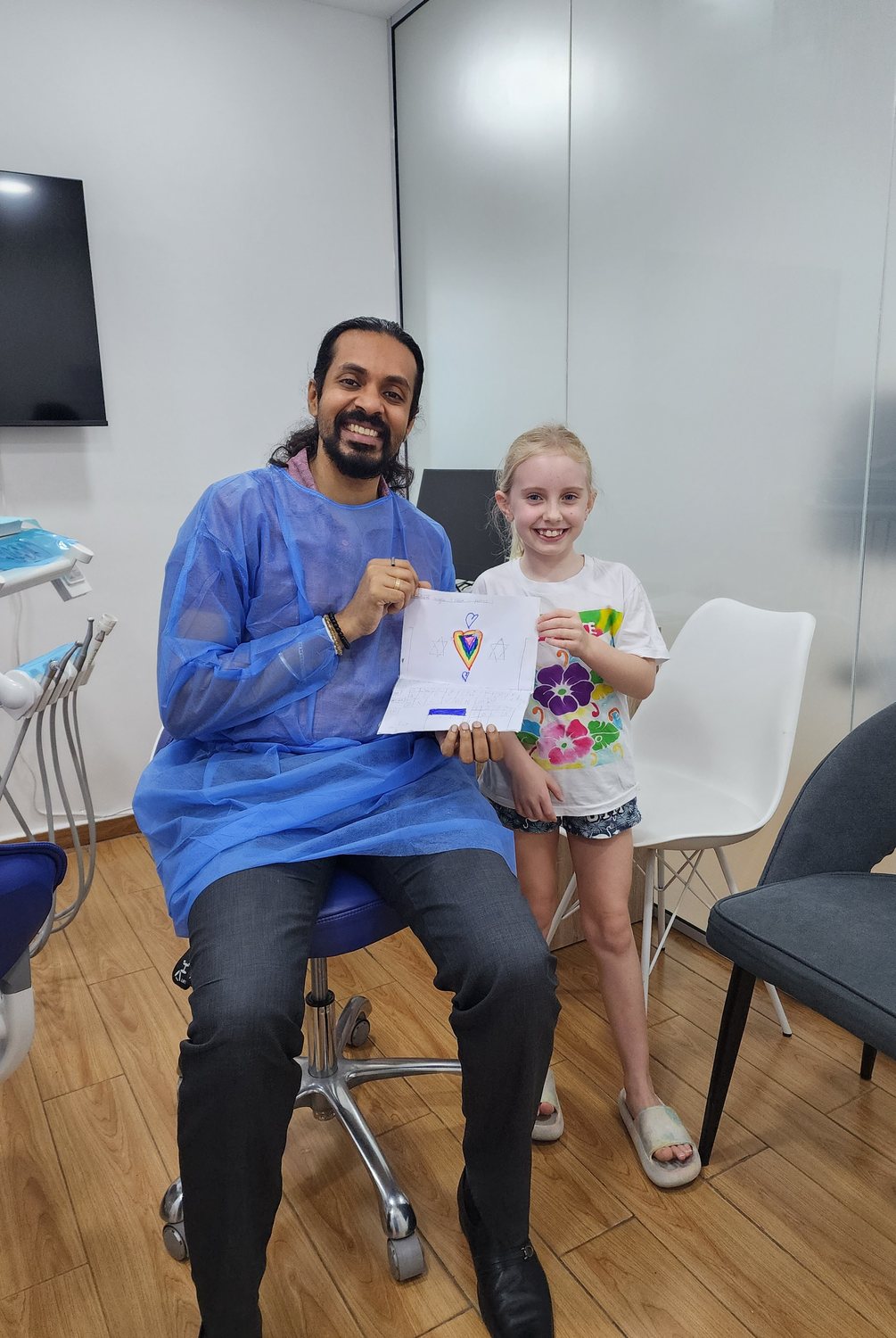 Dr. Keerthan with a young patient holding a thank-you drawing